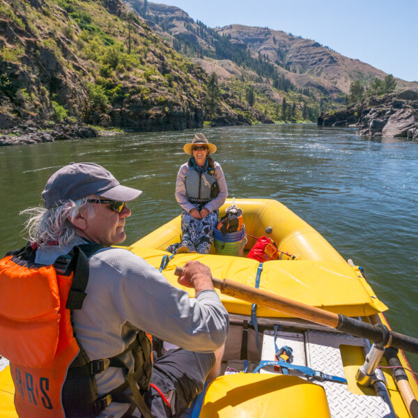 A training guide sits on the front of the raft and watches as a guest rows the raft with oars
