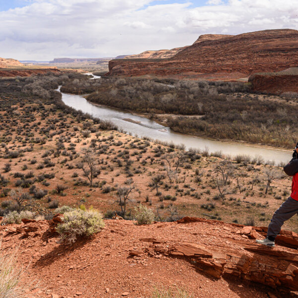 A hiker stands on a rocky formation high above the San Juan River and takes in the expansive view.
