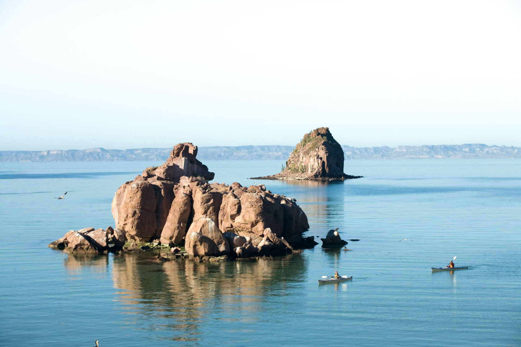People sea kayaking next to large rocks in the ocean.