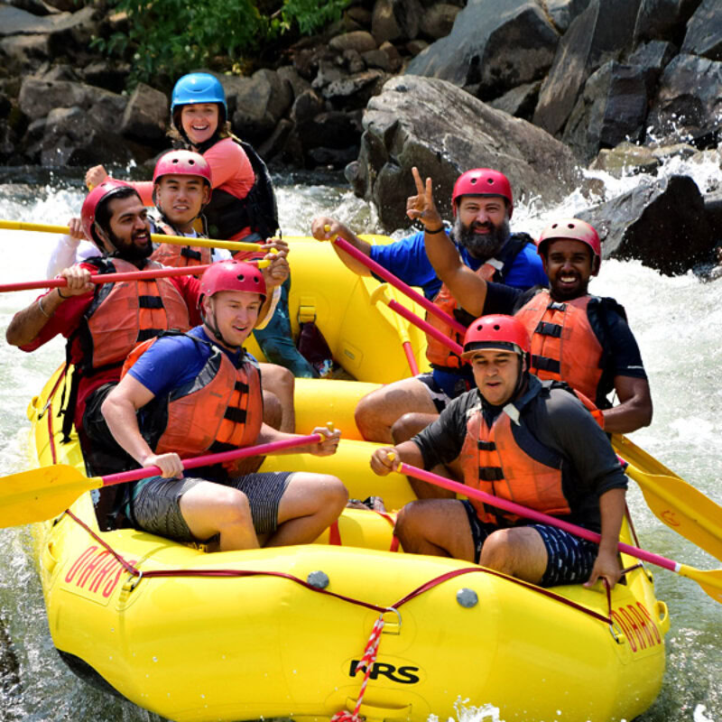 A group of ecstatic paddlers in a yellow raft smile for the camera as they enter a rapid on the South Fork American River.