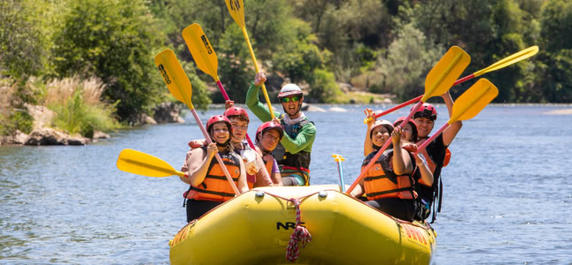 A group rafting on the South Fork of the American River raises their paddles.