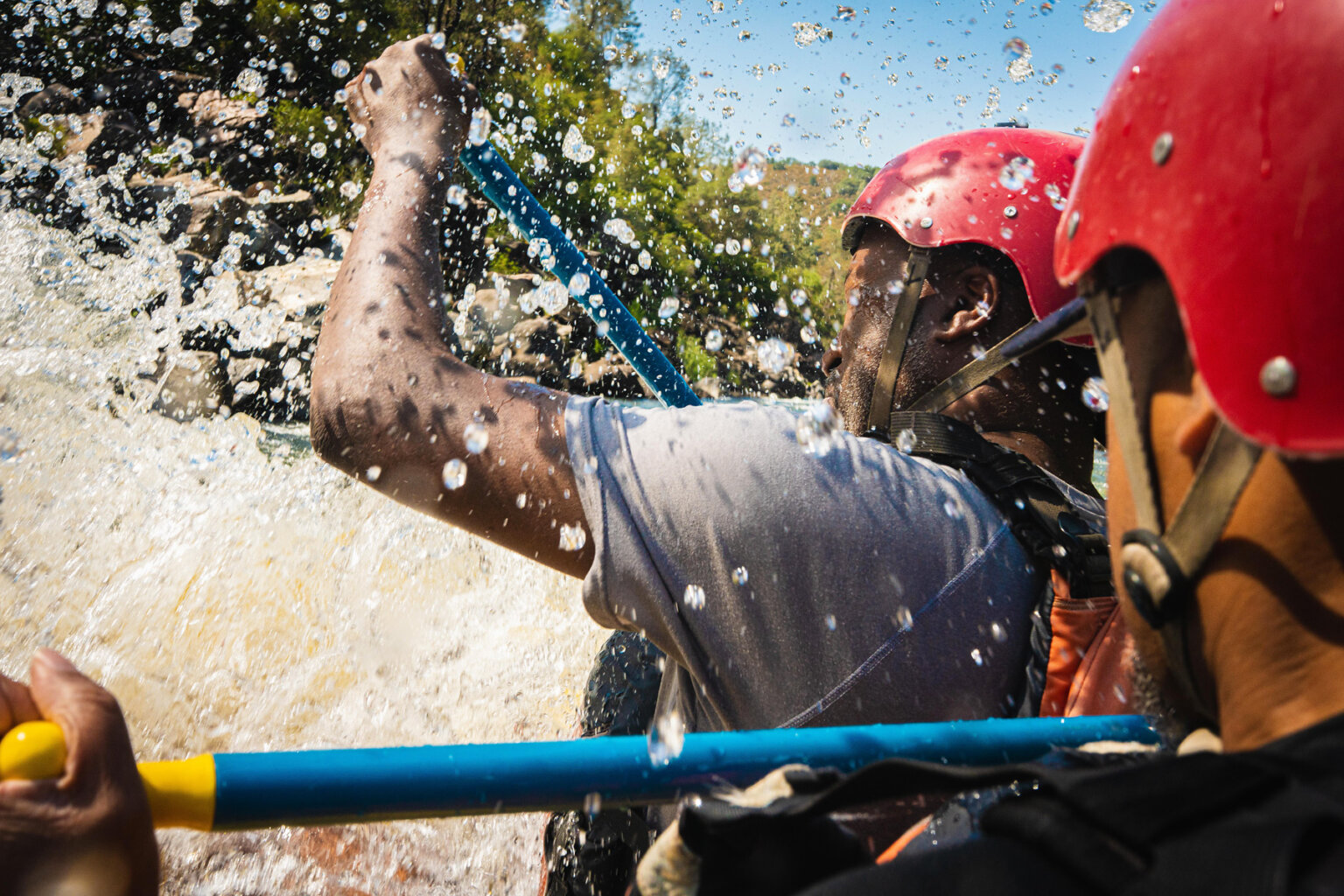 Close-up over the shoulder shot of two paddlers as they get splashed by water going through a rapid.
