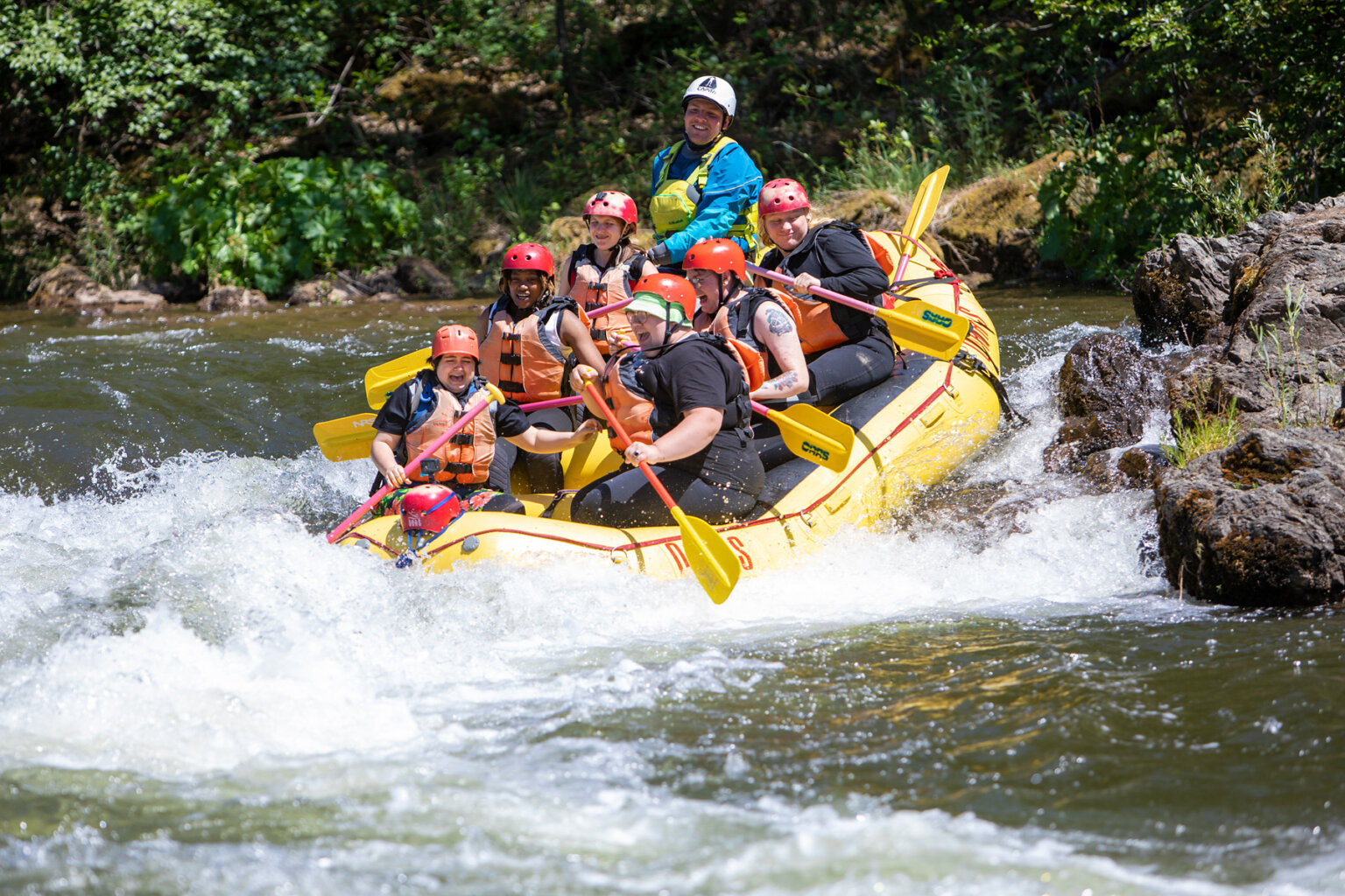 A yellow raft with six paddlers and a guide enter a rapid on the South Fork American River.