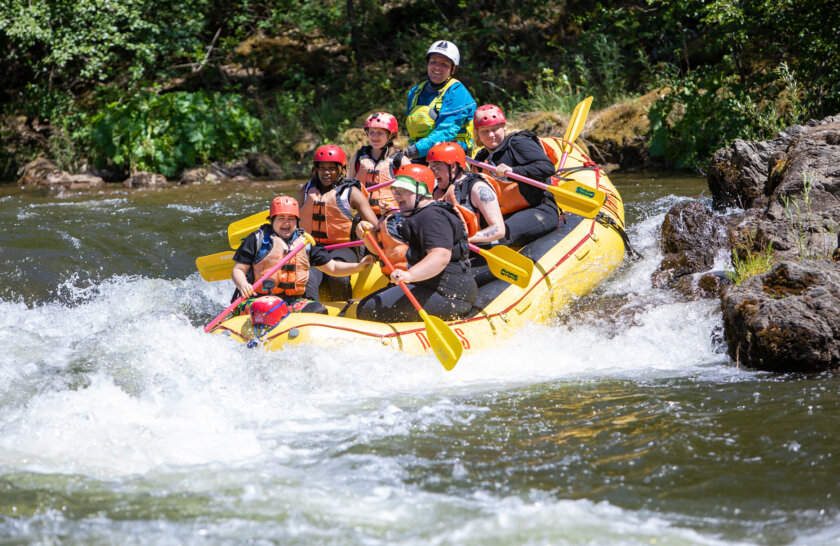 A yellow raft with six paddlers and a guide enter a rapid on the South Fork American River.