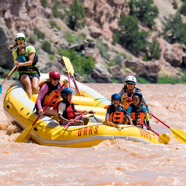 Three ecstatic children in the front of a paddle raft with two adults and a guide behind them as they paddle through a small rapid on the Green River.
