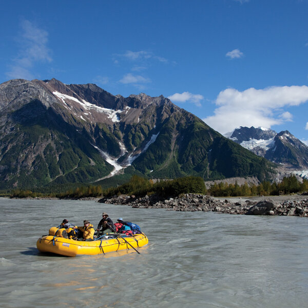 A yellow raft on the Tatshenshini River with mountains behind in Alaska