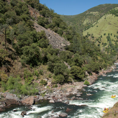 Landscape view of three yellow rafts and a catamaran on an OARS Tuolumne River trip in California.