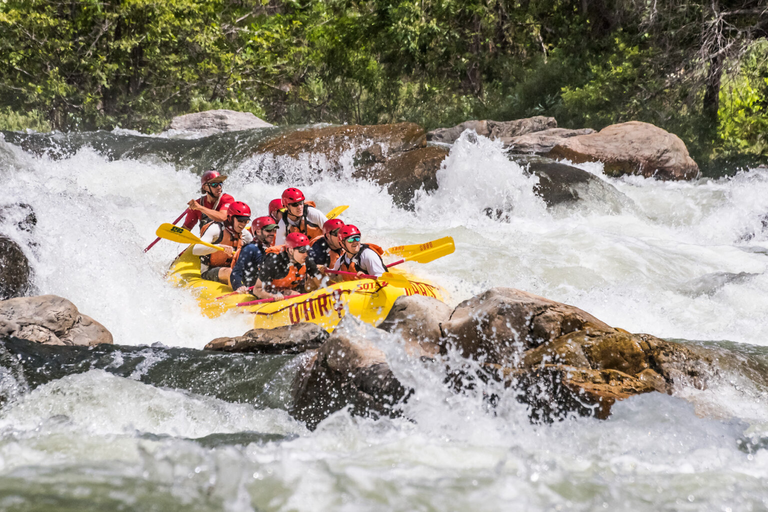 A group of guests and a guide paddle through boulder strewn whitewater on the Tuolumne River in California.
