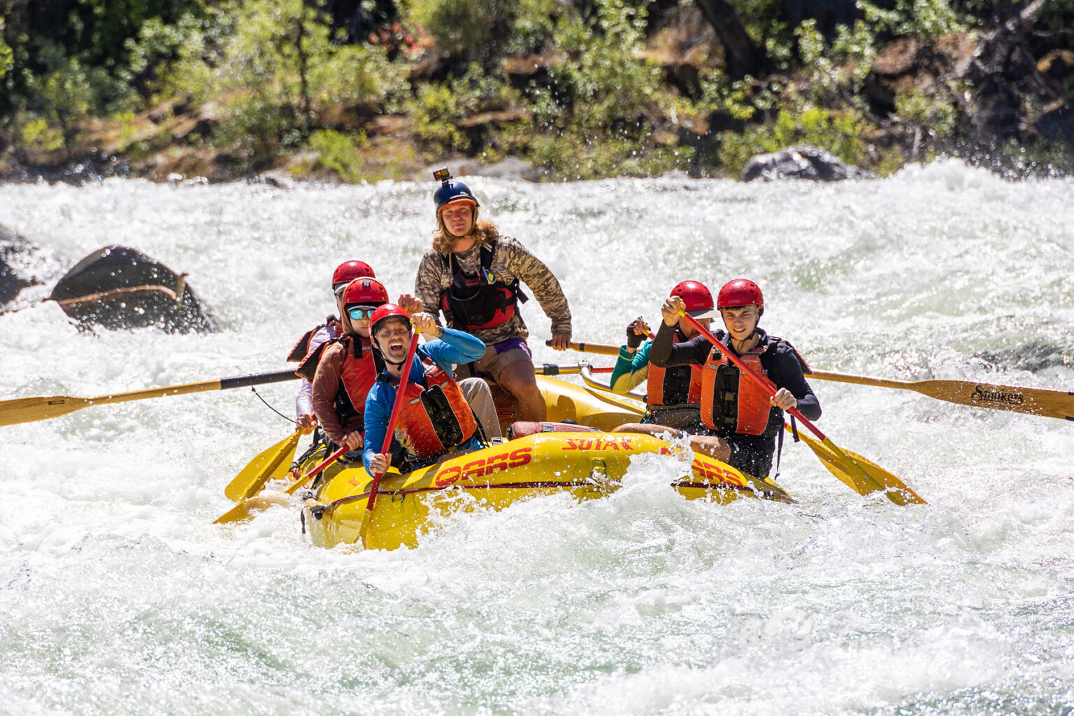 A yellow raft of paddlers surounded by frothy whitewater as they make their way through a rapid on the Tuolumne River in California