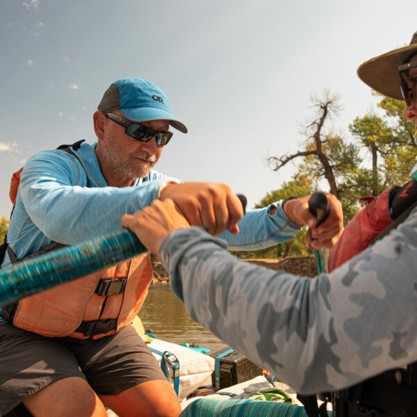 A man holding onto oars as a training guide helps adjust his technique.