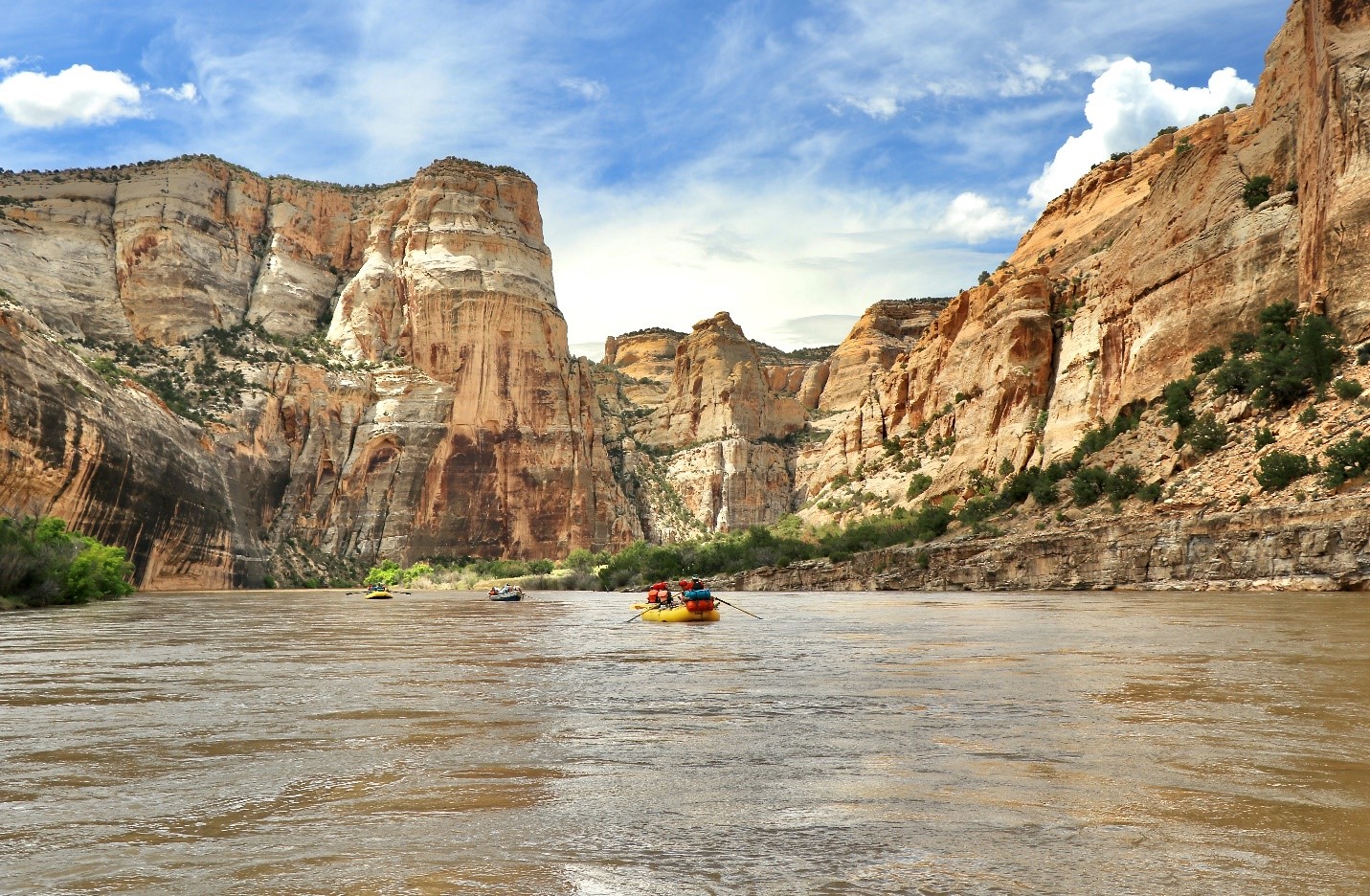 Two rafts and a dory make their way downstream on the Yampa River as massive canyon walls tower above them.